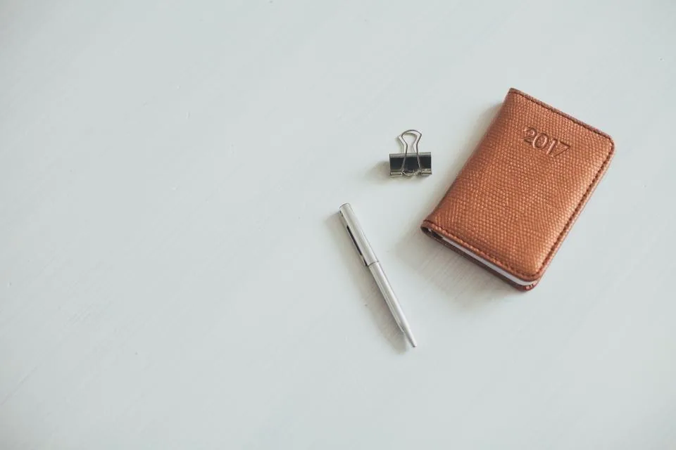 a planner, a notebook and a pen laid out on a desk