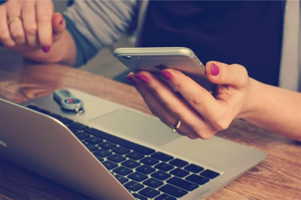 a laptop open on a desk beside a notebook, a phone and a cup of coffee