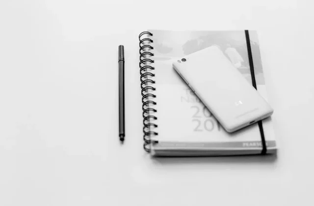a notebook open on a desk with a pen, a phone and printed sheets beside it