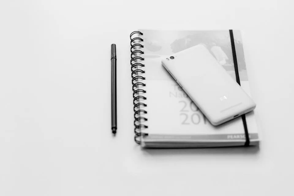 a notebook open on a desk with a pen, a phone and printed sheets beside it