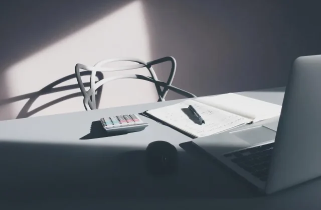 a notebook open on a desk with a pen, a phone and printed sheets beside it