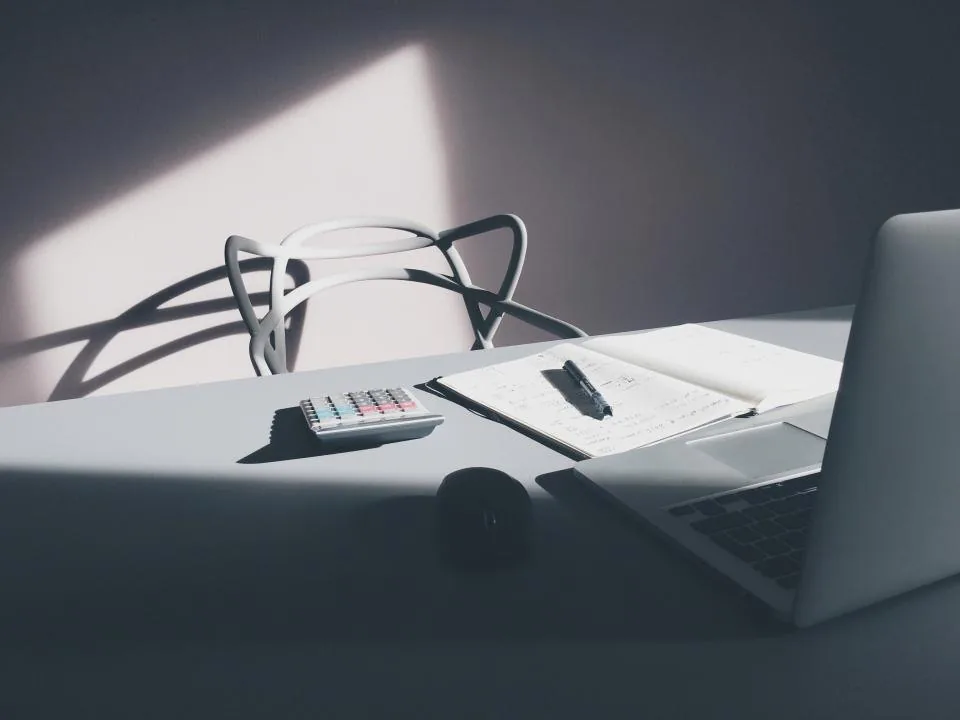 a notebook open on a desk with a pen, a phone and printed sheets beside it