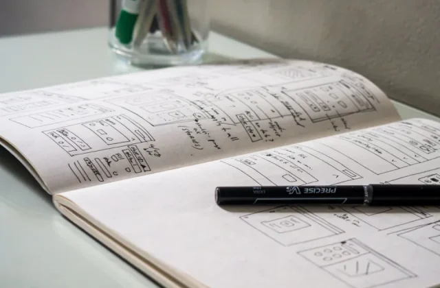 a notebook open on a desk with a pen, a phone and printed sheets beside it