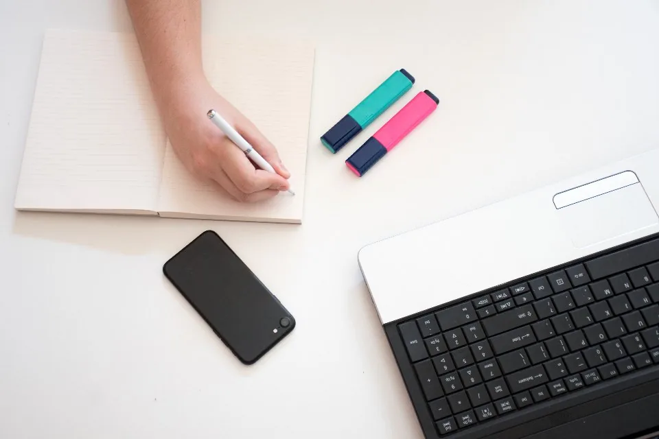 a notebook open on a desk with a pen, a phone and printed sheets beside it
