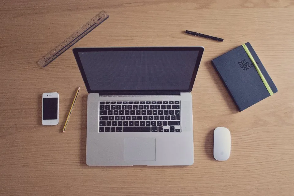 a close view of a desk with a keyboard, a notebook, a pen and a coffee cup