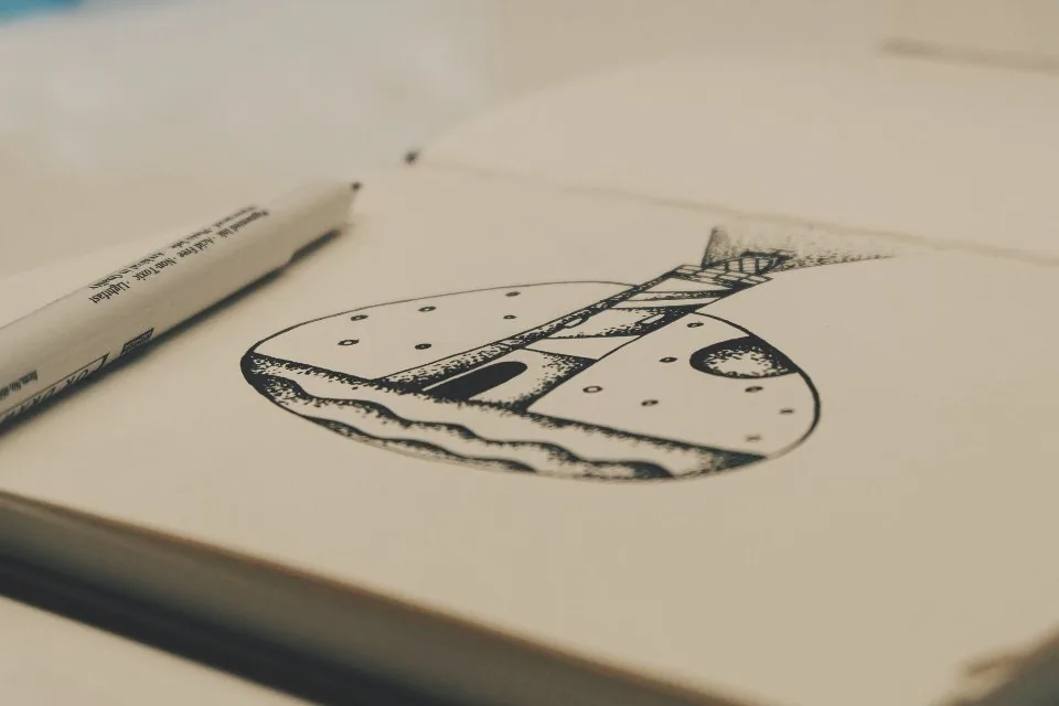 a page of interface sketches on paper beside a laptop and a pen