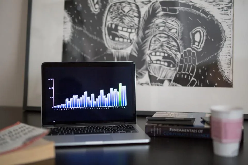 a laptop showing a financial report beside a notebook, a calculator and a phone