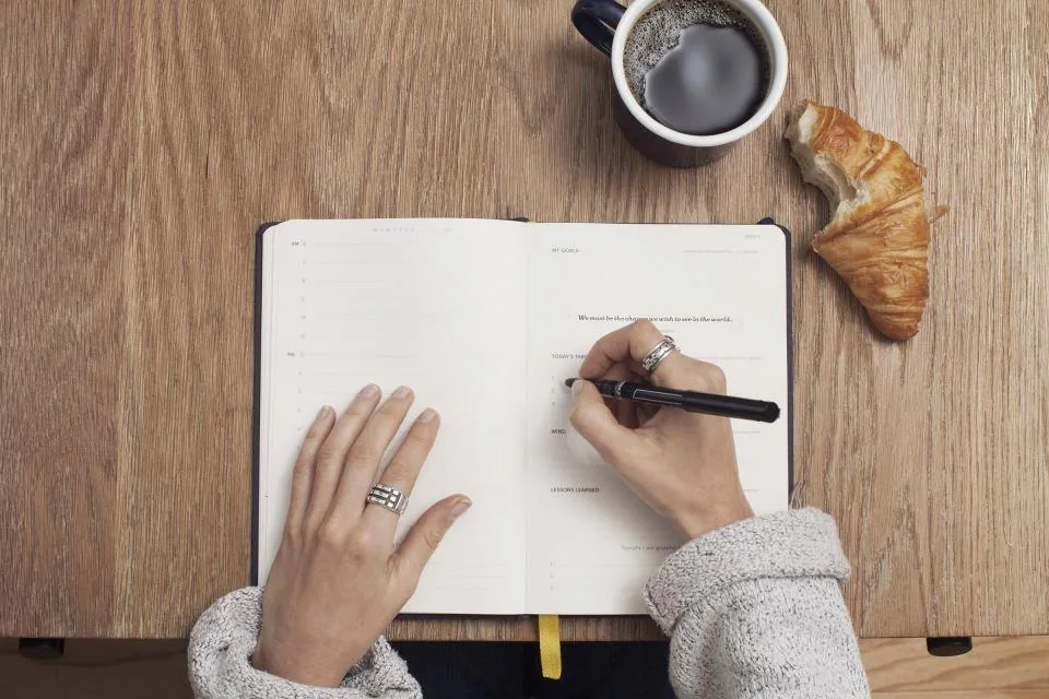 a spiral notebook and pen laid out on a wooden desk