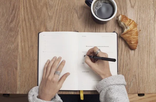 a notebook open on a desk with a pen, a phone and printed sheets beside it