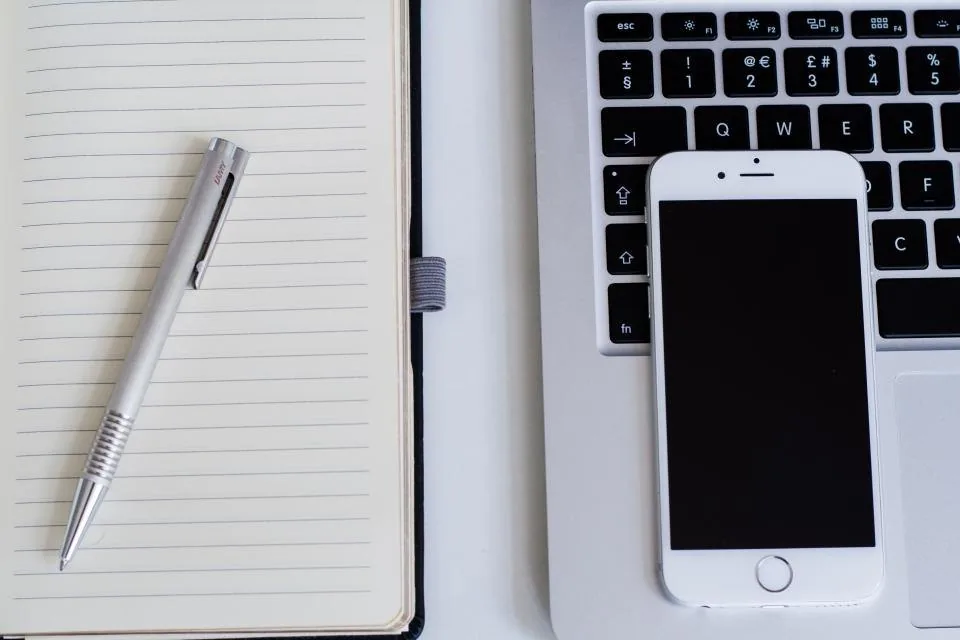 a notebook open on a desk with a pen, a phone and printed sheets beside it