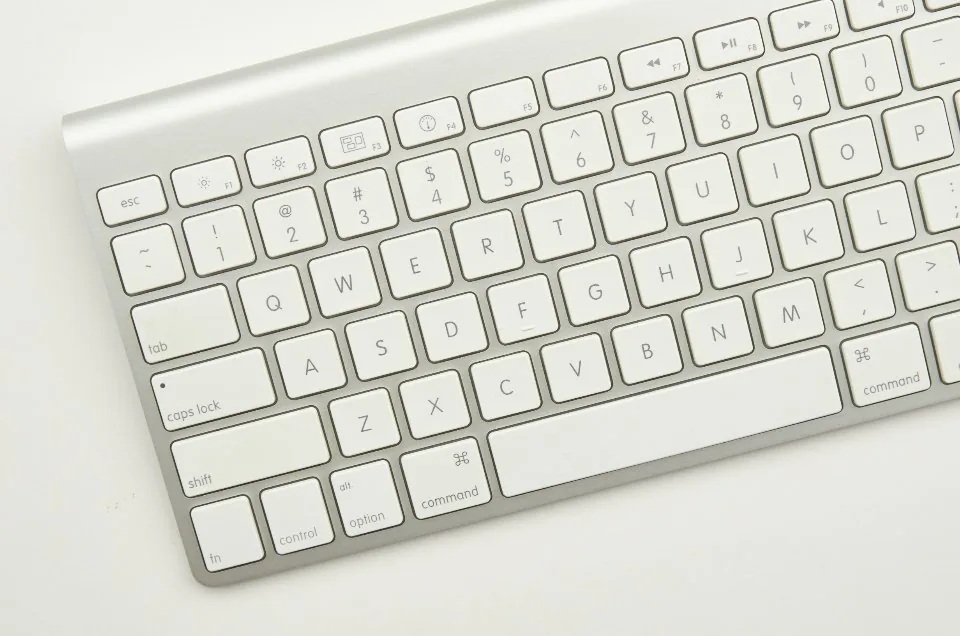 a close view of a desk with a keyboard, a notebook, a pen and a coffee cup