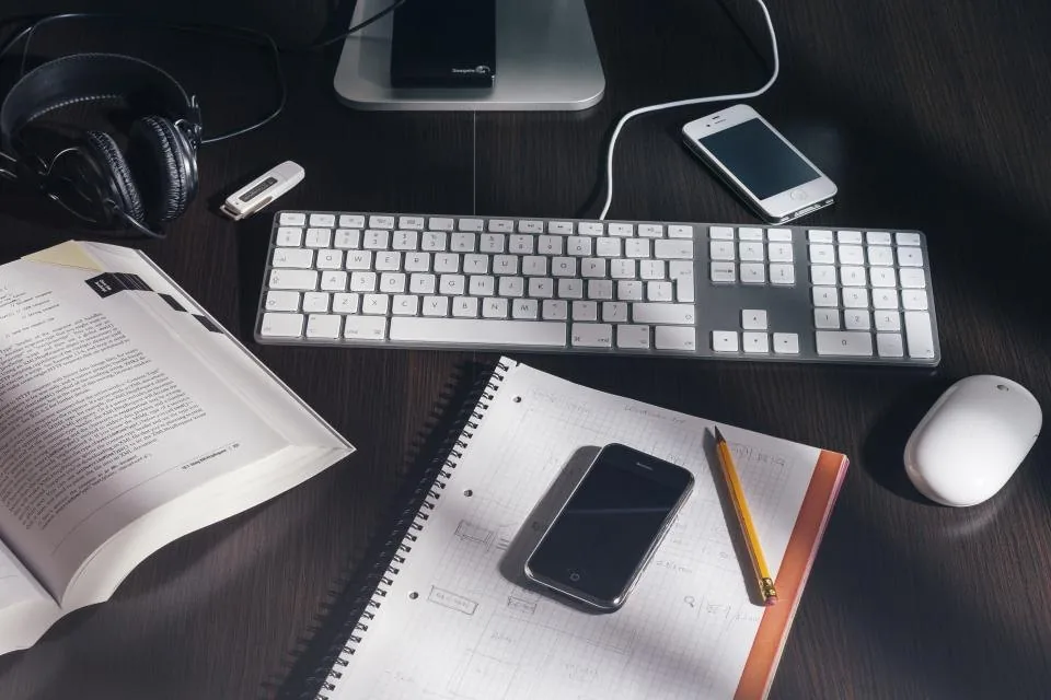 a close view of a desk with a keyboard, a notebook, a pen and a coffee cup