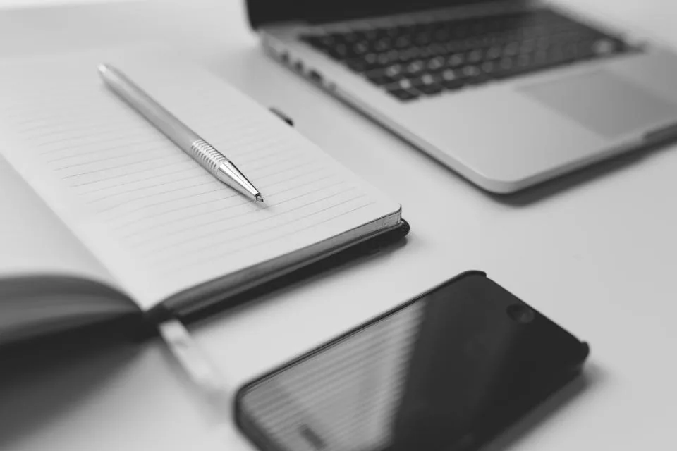 a close view of a desk with a keyboard, a notebook, a pen and a coffee cup