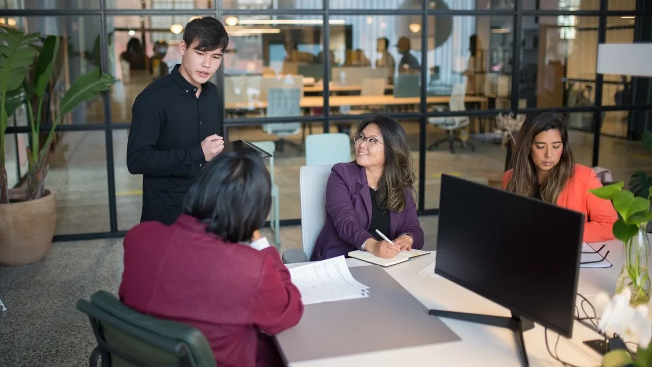 Colleagues in discussion around a table in a bright meeting room.
