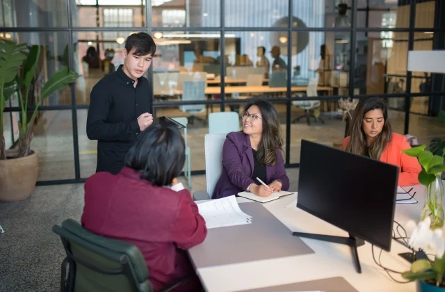 Colleagues in discussion around a table in a bright meeting room.