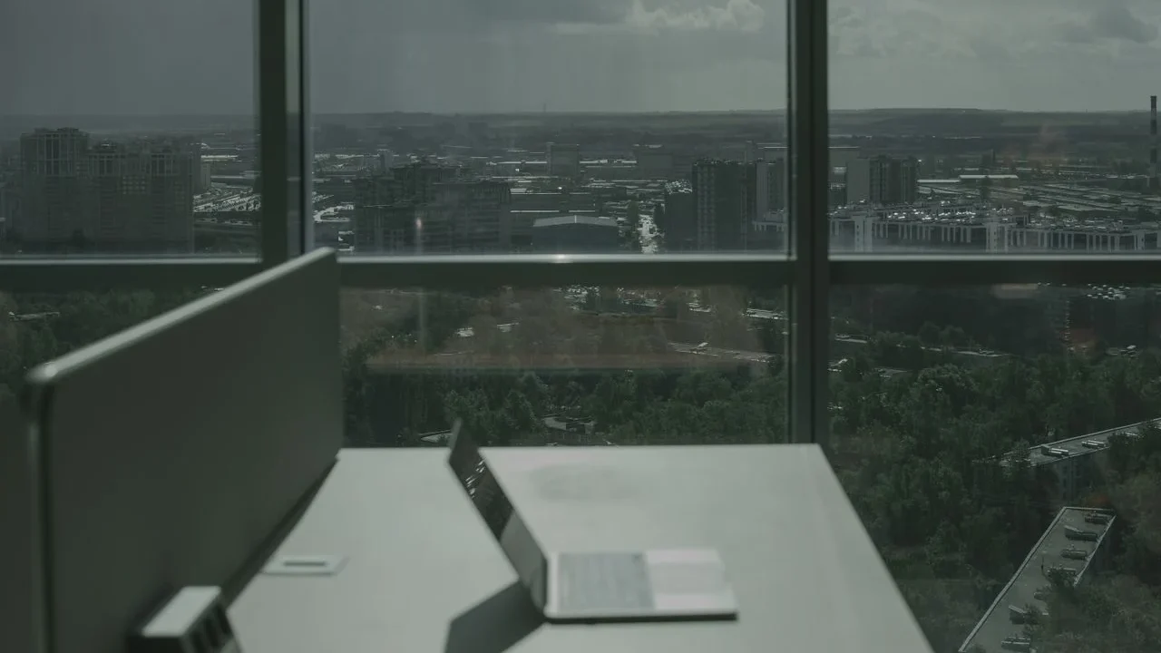A laptop on a desk beside a large window looking out over a city skyline.