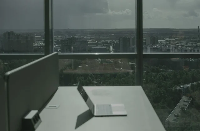 A laptop on a desk beside a large window looking out over a city skyline.