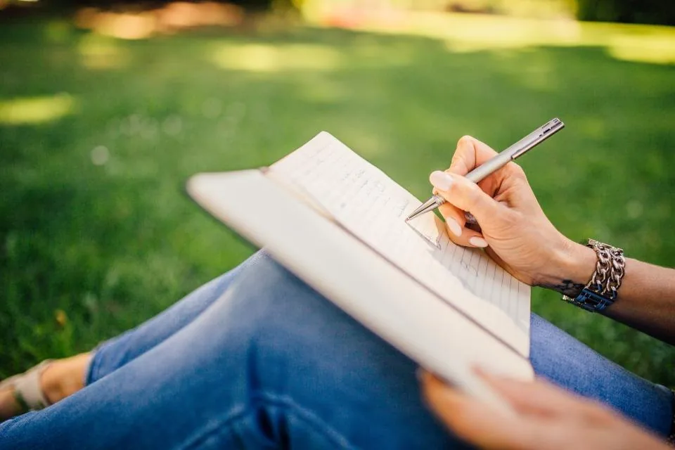 a hand writing notes in a notebook on a desk beside a laptop