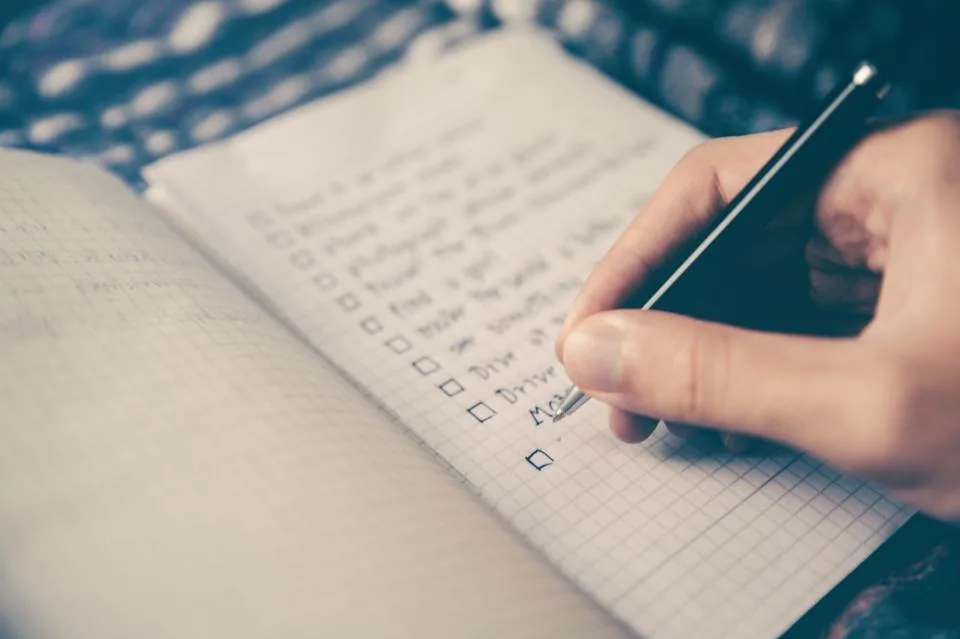 a hand writing notes in a notebook on a desk beside a laptop