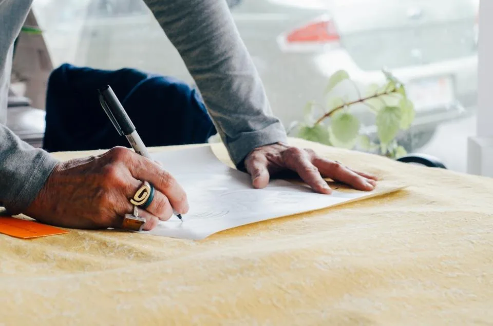 a hand writing notes in a notebook on a desk beside a laptop