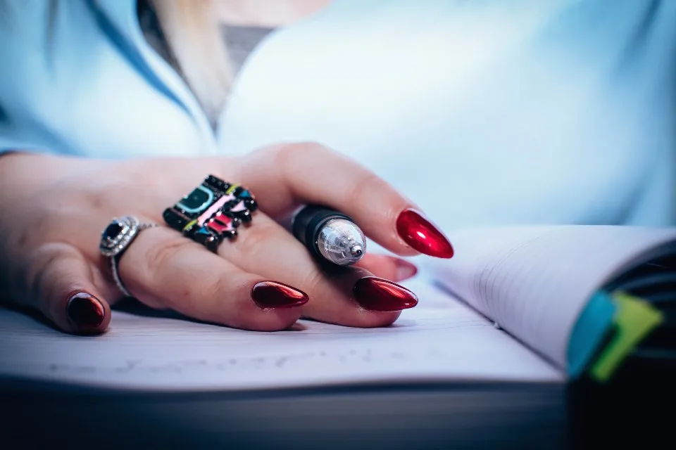 a hand writing notes in a notebook on a desk beside a laptop