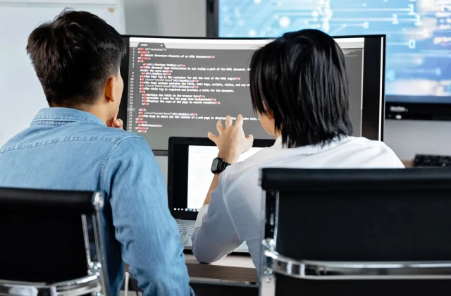 Two developers reviewing application code together on a screen in an office.