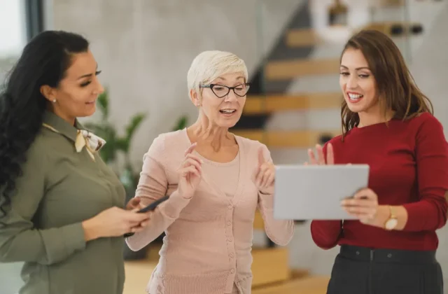Three colleagues talking through an idea in a bright office, one holding a tablet.