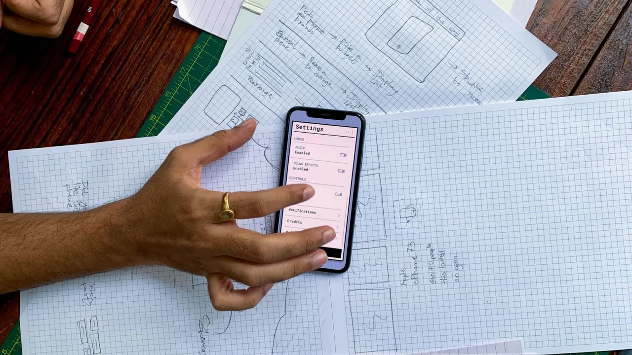 A developer sketching a mobile app interface beside a smartphone.