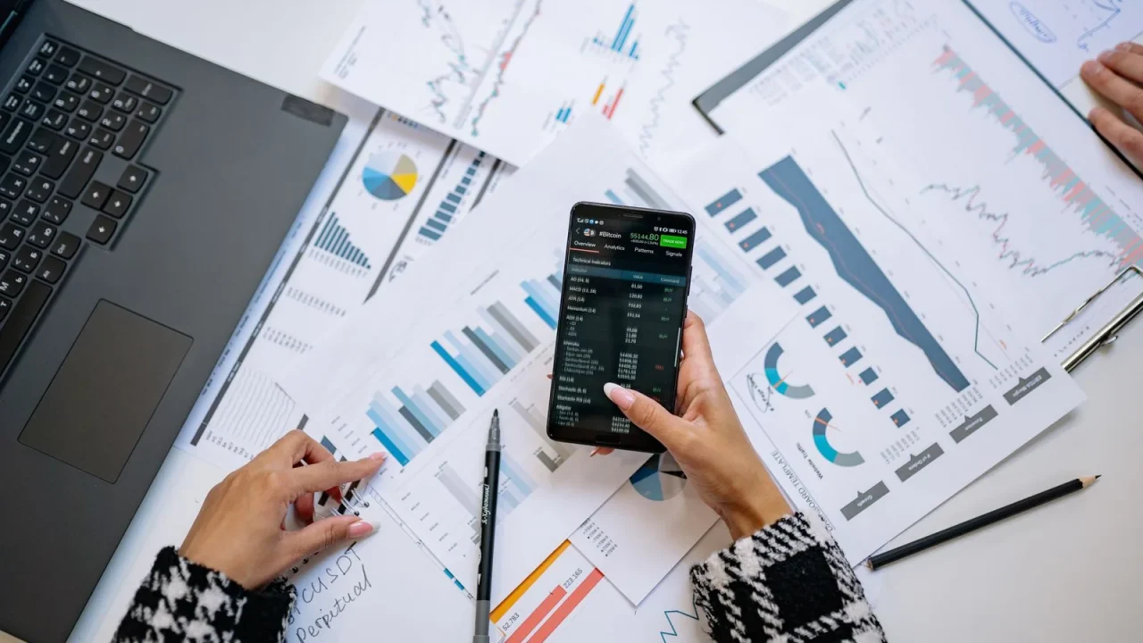 A person reviewing business charts and reports on a laptop and phone.