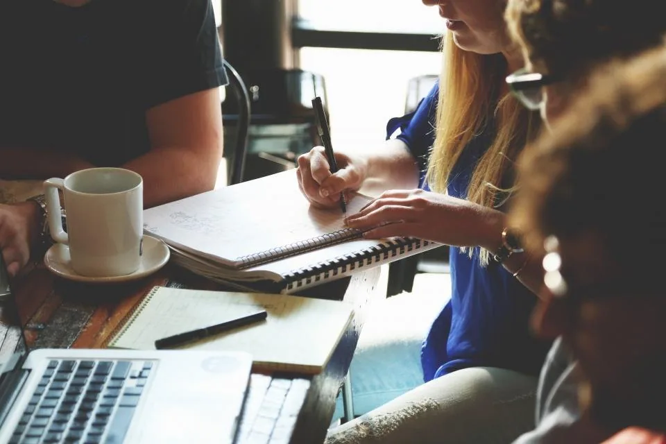 hands working together over a laptop and notes at a table
