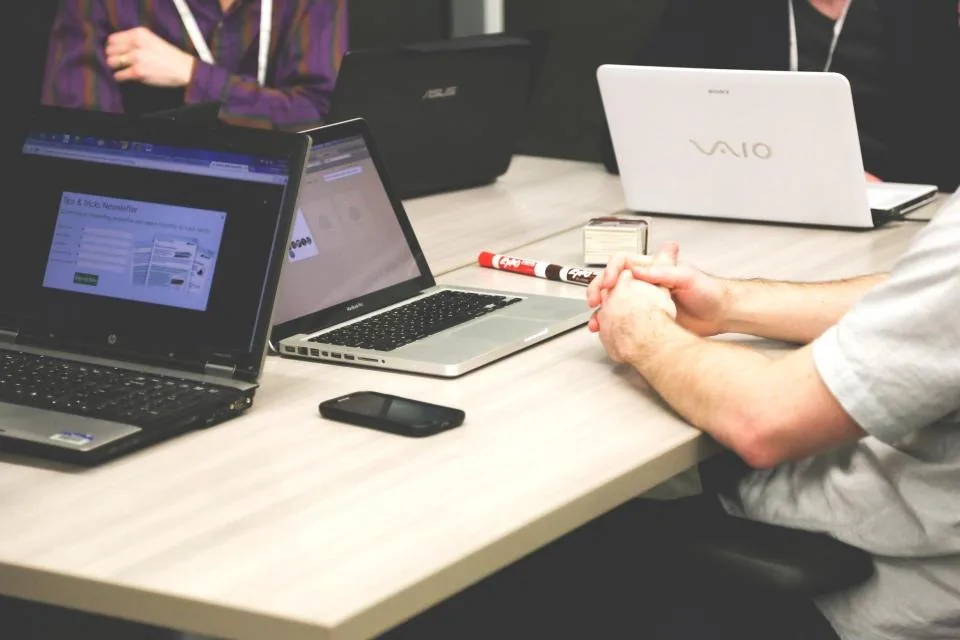 hands working together over a laptop and notes at a table