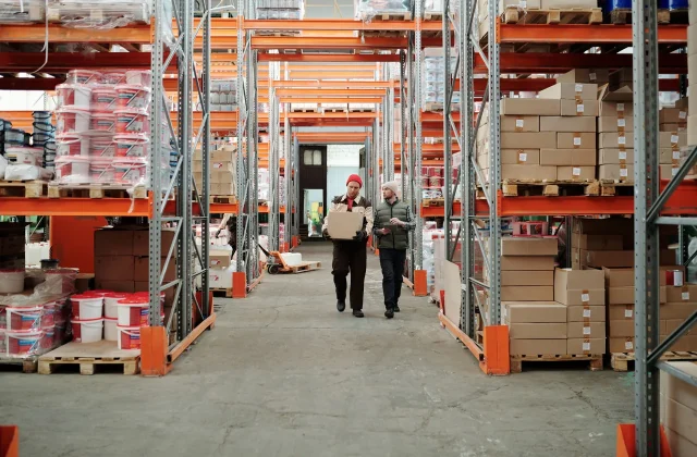 Warehouse staff walking a long aisle between packed storage racks.