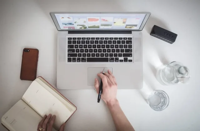a notebook open on a desk with a pen, a phone and printed sheets beside it