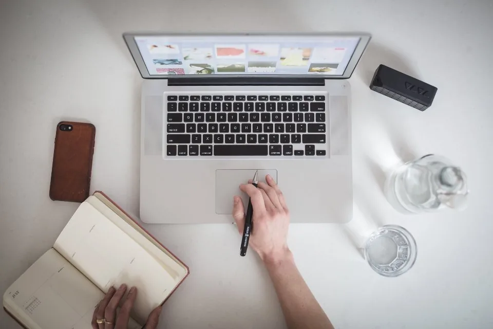a notebook open on a desk with a pen, a phone and printed sheets beside it